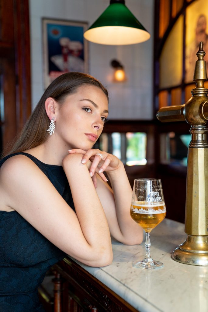 a girl standing at a bar wears Guinnot earrings from the One-off collection. Next to her is a glass of beer.